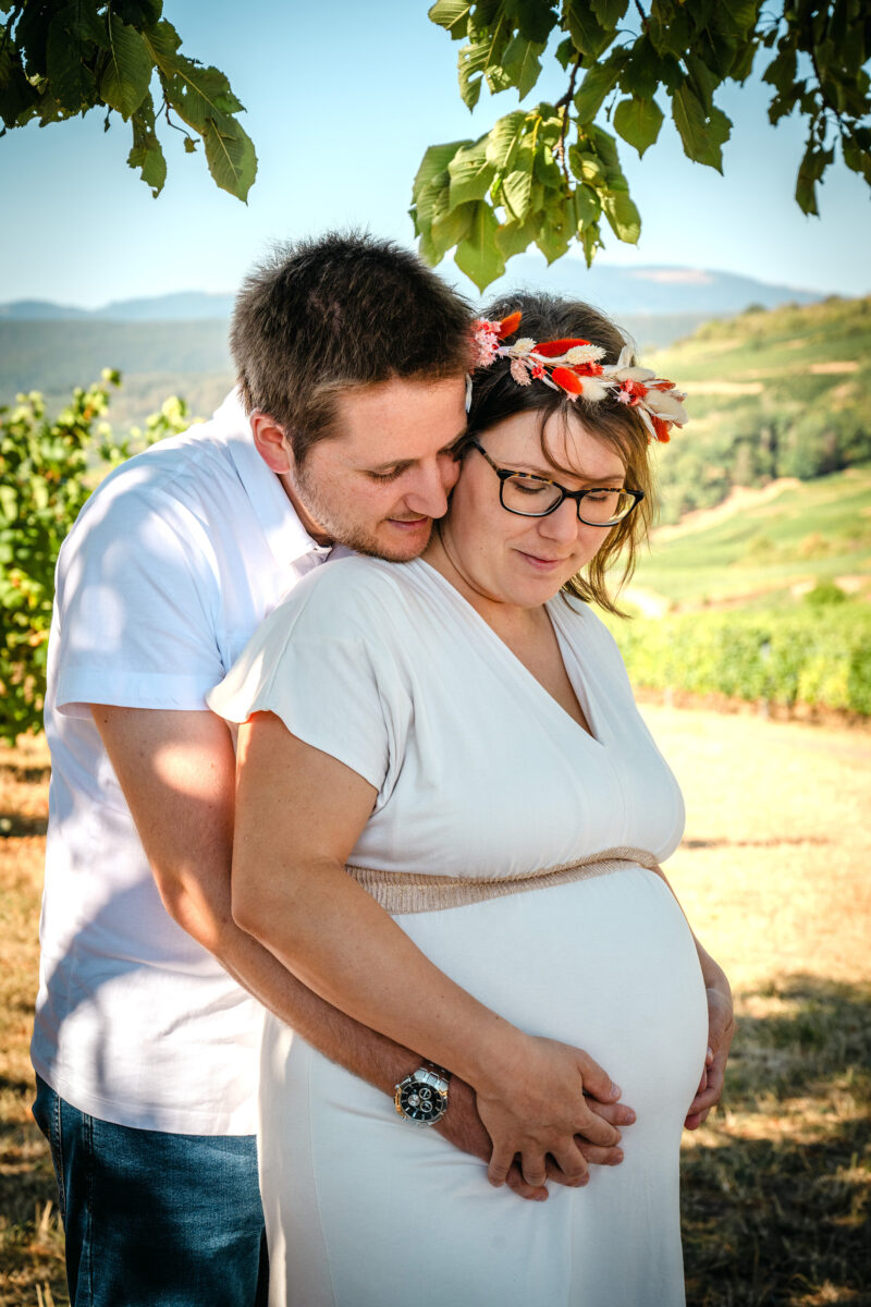 Couple enlacé dans les vignes pendant une séance photo grossesse.