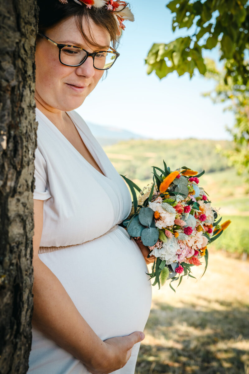 Séance photo grossesse avec une femme devant un arbre et son bouquet de fleurs
