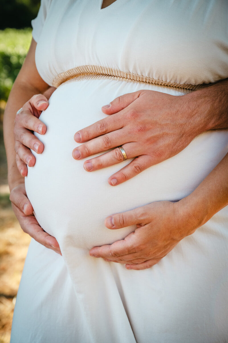 Couple qui posent leurs mains sur ventre de femme enceinte pendant une séance photo